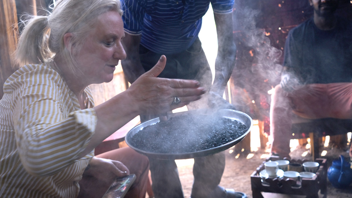 Alice participating in Ethiopian coffee ceremony, inhaling blessed coffee aroma with hands cupped over roasted beans