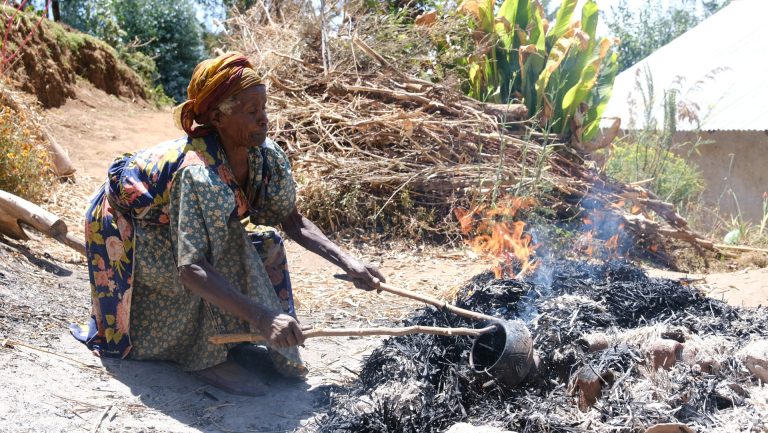 Ethiopian potter in colorful traditional dress retrieving fired clay jebena coffee pot from traditional outdoor kiln using long wooden tools